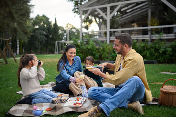 Happy young family sitting on blanket and having take away picnic outdoors in restaurant area.