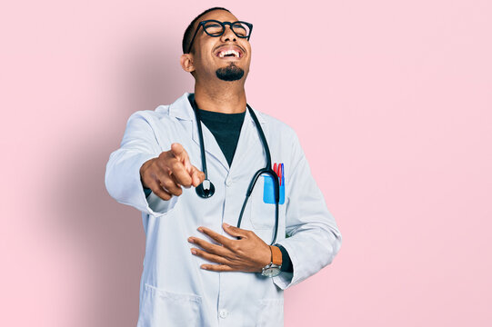 Young african american man wearing doctor uniform and stethoscope laughing at you, pointing finger to the camera with hand over body, shame expression