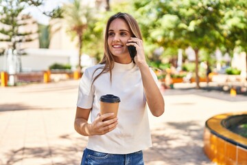 Young blonde woman talking on the smartphone and drinking coffee at park