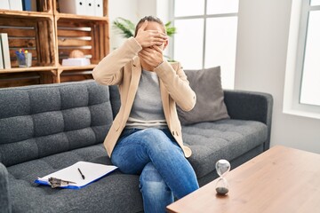 Obraz premium Young woman working at consultation office covering eyes and mouth with hands, surprised and shocked. hiding emotion