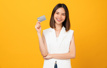 Cheerful beautiful Asian woman holding mockup credit card on yellow background.
