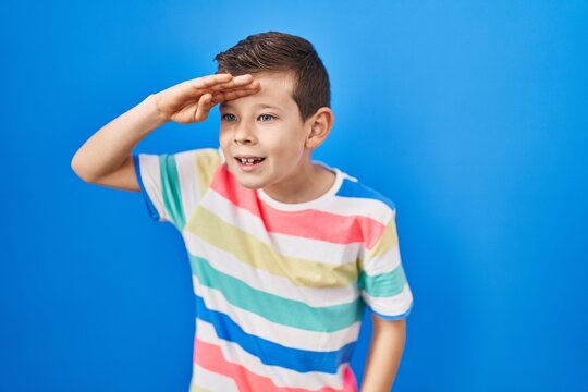 Young caucasian kid standing over blue background very happy and smiling looking far away with hand over head. searching concept.