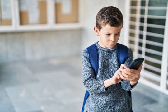 Blond child student using smartphone standing at school