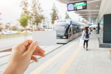 Hand of a passenger holding white empty card for contactless and cashless paying for modern urban transport system in the city