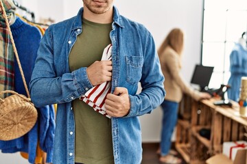 Young hispanic robber man stealing shirt at clothes store.