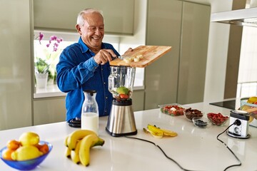 Senior man smiling confident putting banana in blender at kitchen
