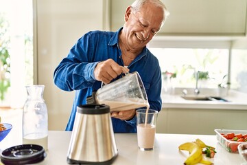 Senior man smiling confident pouring smoothie on glass at kitchen