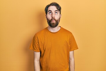 Caucasian man with beard wearing casual yellow t shirt making fish face with lips, crazy and comical gesture. funny expression.
