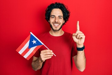 Handsome hispanic man holding puerto rico flag smiling with an idea or question pointing finger with happy face, number one
