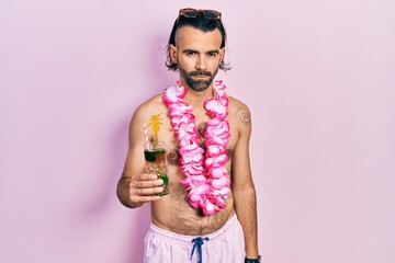 Young hispanic man wearing swimsuit and hawaiian lei drinking tropical cocktail skeptic and...
