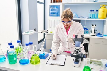 Young hispanic woman wearing scientist uniform analysing blood at laboratory