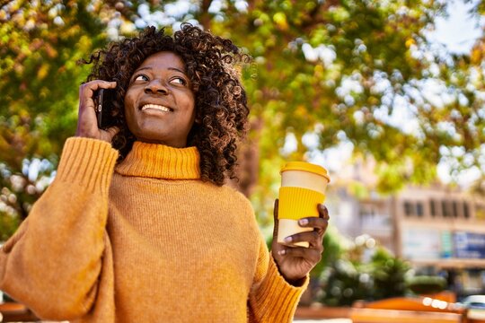 African american woman talking on the smartphone drinking coffee at park