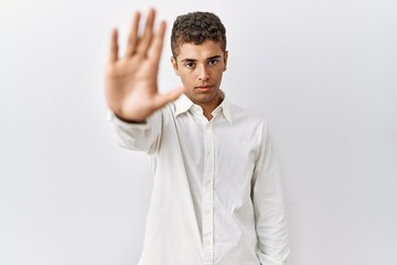 Young handsome hispanic man standing over isolated background doing stop sing with palm of the...