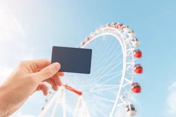 Foto auf Leinwand Hand holding white card as entrance ticket or discount with ferris wheel in amusement luna park © EdNurg