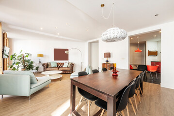 Living room with large wooden dining table and black resin chairs, three-seater sofa and wooden floor