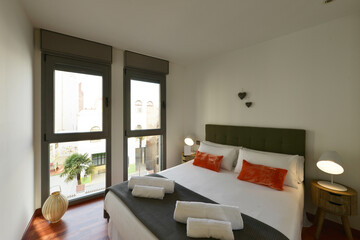 Bedroom with queen bed with cushions and pillows, clean rolled up towels and twin balconies overlooking the street