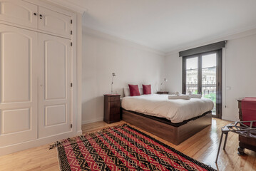 Double bedroom with beautiful decoration in noble wood, white fitted wardrobes, carpets and balcony with glass doors and bronze-colored aluminum