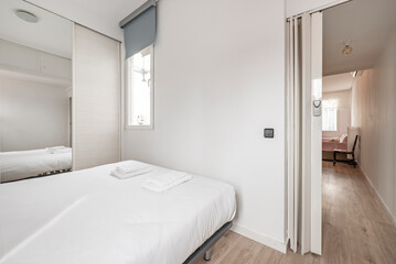 Fototapeta na wymiar Double bedroom with bed with white duvet, wardrobe with Venetian white wooden sliding doors and mirrors