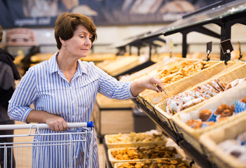 mature woman choosing bread and baking in grocery section of supermarket