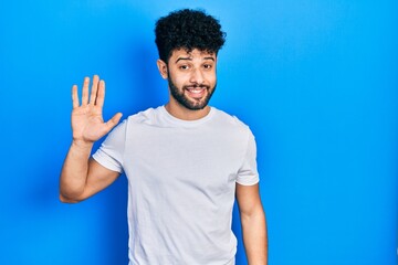 Young arab man with beard wearing casual white t shirt waiving saying hello happy and smiling, friendly welcome gesture