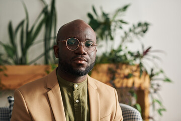 Medium shot of young serious and confident psychoanalyst in formalwear and eyeglasses looking at...