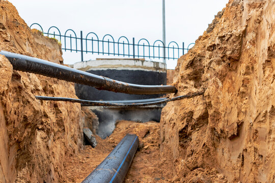 The high voltage electrical cable is laid in a trench under existing engineering sewerage networks. Laying a high voltage cable for supplying buildings with electricity.