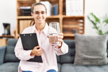 Young hispanic woman holding water having psychologist session at clinic