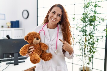 Young redhead pedriatician woman holding teddy bear smiling happy pointing with hand and finger