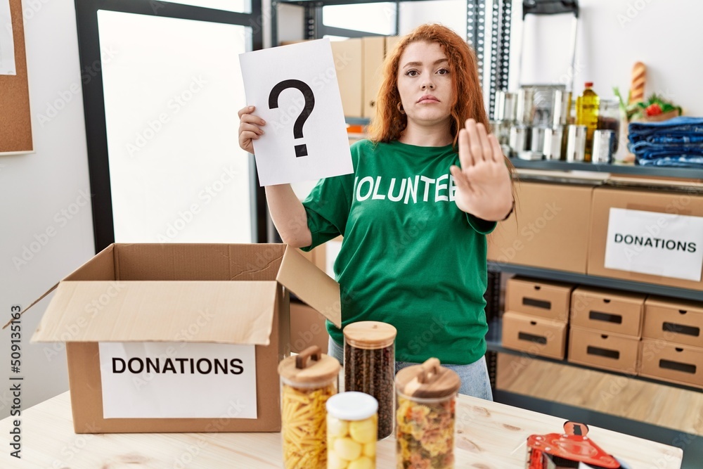 Canvas Prints Young redhead woman wearing volunteer t shirt holding question mark with open hand doing stop sign with serious and confident expression, defense gesture