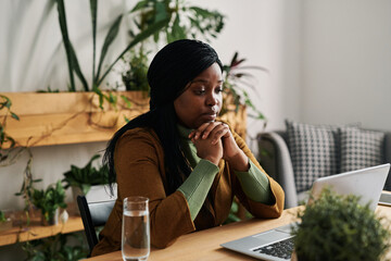 Young female psychoanalyst looking at patient during online session while sitting by her workplace in front of laptop in office