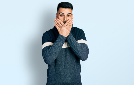 Young hispanic man with beard wearing casual winter sweater shocked covering mouth with hands for mistake. secret concept.