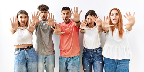 Obraz premium Group of young friends standing together over isolated background doing stop gesture with hands palms, angry and frustration expression