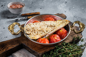 Roasted Haddock fish fillet in skillet with tomato and potato. Gray background. Top view
