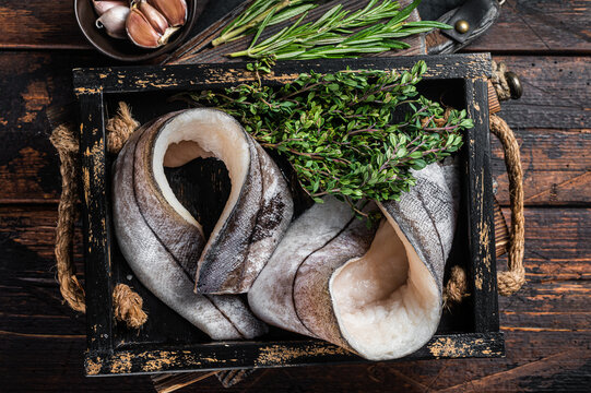 Raw Haddock fish fillets in wooden tray with rosemary and thyme. Wooden background. Top view