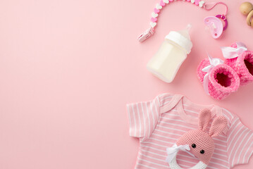 Baby accessories concept. Top view photo of infant clothes pink shirt baby booties pacifier chain knitted bunny rattle toy wooden rattle and bottle on isolated pastel pink background with empty space