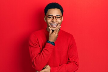 Young african american man wearing casual clothes and glasses looking confident at the camera smiling with crossed arms and hand raised on chin. thinking positive.