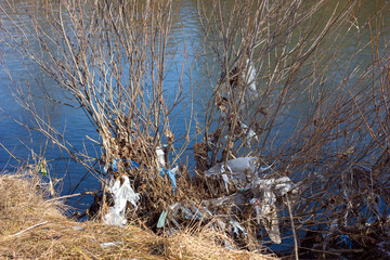 Garbage plastic bottles and plastic bags on the river bank, nature pollution, environmental disaster, selective focus	