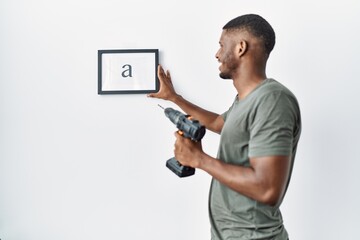 Young african american man hanging frame using drill at home