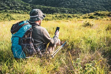 Image of hiker using phone while spending time in nature.	