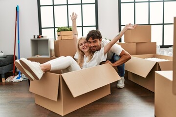 Fototapeta premium Young beautiful couple smiling happy playing using cardboard box as a car at new home.