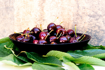 ripe cherries on black dish and green cherry leaves