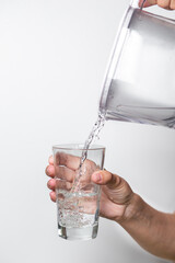 Female hands pour clean water from a filter jug into a glass beaker on a white background.