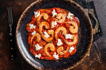 Saganaki Shrimp prawns with tomato and feta cheese on a plate. Dark background. Top view.