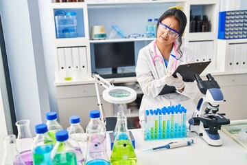 Fototapeta premium Young chinese woman wearing scientist uniform writing on document at laboratory