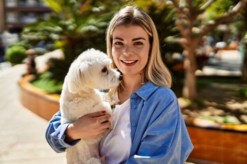 Young blonde girl smiling happy holding dog at the city.