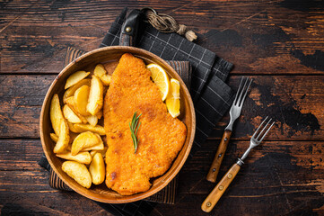 Austrian fried weiner schnitzel with potato wedges in a wooden plate. Wooden background. Top view - obrazy, fototapety, plakaty