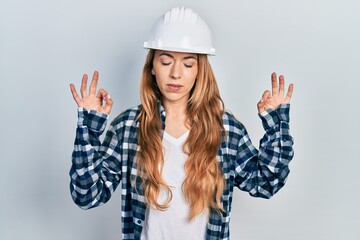 Young caucasian woman wearing architect hardhat relax and smiling with eyes closed doing meditation gesture with fingers. yoga concept.
