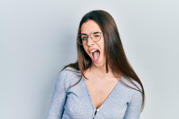 Obraz premium Young brunette teenager wearing casual sweater and glasses winking looking at the camera with sexy expression, cheerful and happy face.