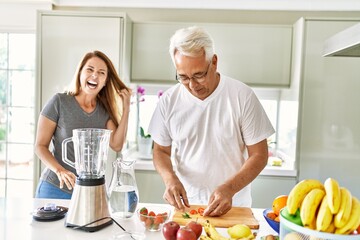 Middle age hispanic couple smiling happy cooking smoothie at the kitchen.