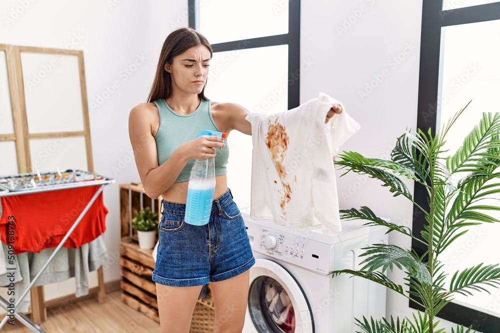 Canvas Prints Young hispanic woman cleaning dirty white t shirt with stain at laundry room skeptic and nervous, frowning upset because of problem. negative person.